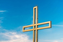 Golden Cross Against A Background Of Blue Sky With Clouds. A Minimalistic View Of A Gold-colored Cross Against The Sky.