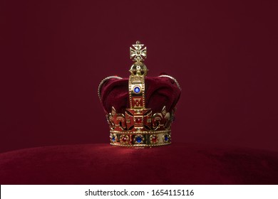 Golden crown on a velvet cushion on a deep red background with copy space