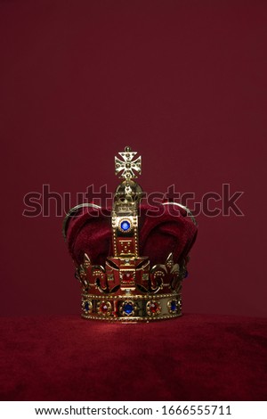 Golden crown on a velvet cushion on a deep red background with copy space in a vertical image