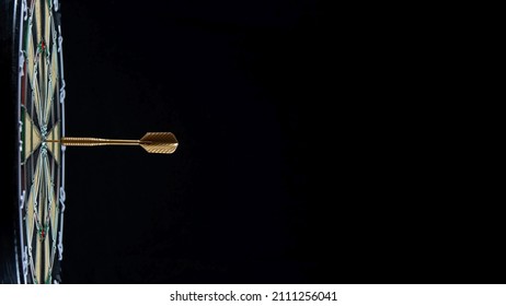 Golden dart arrow in the bullseye of a dart board against a black background