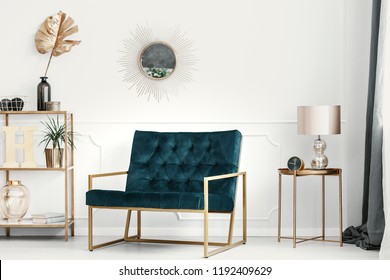 Golden decorations and furniture in an expensive living room interior with an emerald green sofa by a white wall with molding