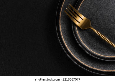 The golden dinner fork is placed on a ceramic dinner plate. The background is black leather. Luxurious, sumptuous fine tableware.Flat lay, top view, banner,horizontal photo - Shutterstock ID 2218687079