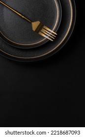 The golden dinner fork is placed on a ceramic dinner plate. The background is black leather. Luxurious, sumptuous fine tableware.Flat lay, top view, vertical photo - Shutterstock ID 2218687093