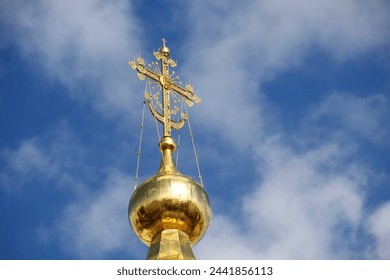 Golden dome of the Orthodox Church with a cross against the blue sky with white clouds. Christian temple