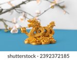 Golden dragon figurine and blooming tree branches on blue table against white background. Chinese New Year celebration
