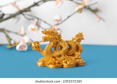 Golden dragon figurine and blooming tree branches on blue table against white background. Chinese New Year celebration