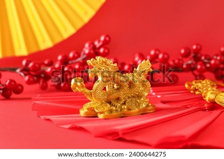Golden dragon figurine with traditional paper fans and berries on red background. Chinese New Year celebration