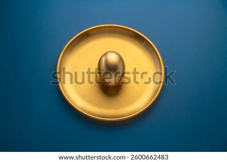 Golden easter egg placed on a golden plate on a blue background, representing luxury, celebration, and the festive spirit of easter, perfect for greeting cards or holiday promotions