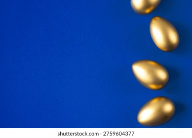 Golden Easter eggs in row over solid deep blue background. Flat lay composition with copy space for text