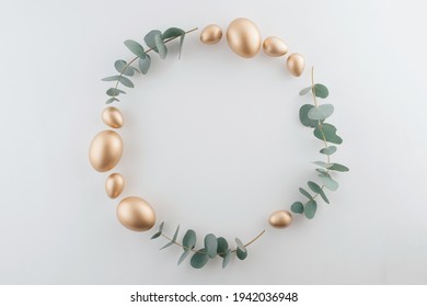 Golden Eggs With Green Eucalyptus Leaves Circle Frame. Easter Decoration Pastel White Background. Top View Square