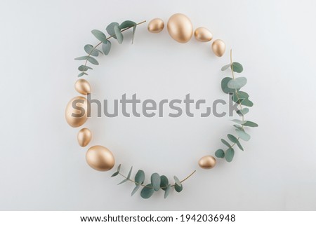 Golden eggs with green eucalyptus leaves circle frame. Easter decoration pastel white background. Top view square