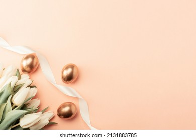 Golden eggs with spring white tulips on pastel pink background in Happy Easter decoration. Foil minimalist egg design, modern top view banner design