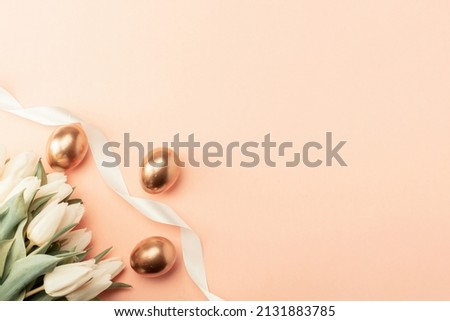 Golden eggs with spring white tulips on pastel pink background in Happy Easter decoration. Foil minimalist egg design, modern top view banner design
