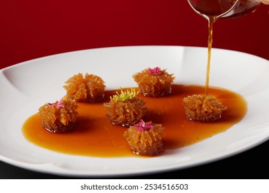 Golden flower-shaped fritters with delicate pink and yellow petals, drenched in amber syrup on a pristine white plate against a deep red backdrop. - Powered by Shutterstock