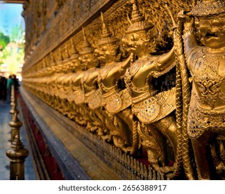 Golden Garuda statues lining the outer wall of the Temple of the Emerald Buddha (Wat Phra Kaew) in Bangkok, Thailand. Traditional Thai craftsmanship and intricate details in a sacred and iconic landma