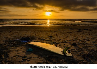 Golden glow of sun setting on beach shines light on yellow surfboard left on sand at Cardiff Beach near San Diego, California.
