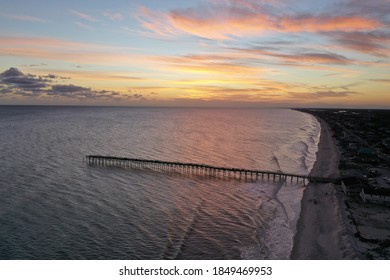 The golden glow of the sunset at Oak Island Pier. Aerial view of the ocean waves along the beach.