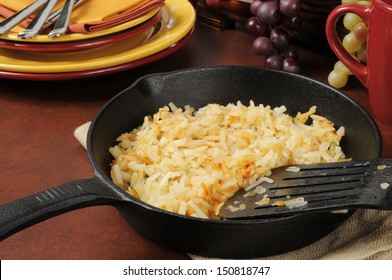 Golden Hash Browns In A Cast Iron Skillet Near Serving Plates And Silverware