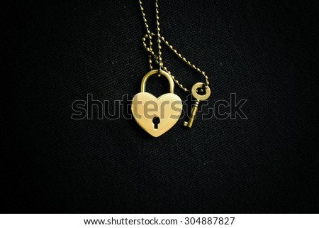 Golden heart and key pendant on black background. Abstract of love.