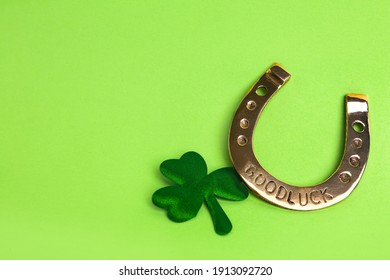 Golden horseshoe and decorative clover leaf on light green background, space for text. Saint Patrick's Day celebration