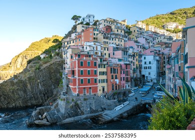 As the golden hour envelops the cliffside, charmingly colorful homes rise above the sparkling harbor of Cinque Terre. Riomaggiore in Cinque Terre, Italy - Powered by Shutterstock