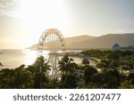 Golden hour over the ferris wheel, treetops, lagoon and hilly backdrop of Cairns Esplanade - Coral Sea, Cairns; Far North Queensland, Australia