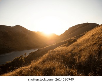 Golden hour soft light sun rays backlight rolling hills green grass farm meadow pasture mountain landscape at Kaihoka Lakes Tasman South Island New Zealand