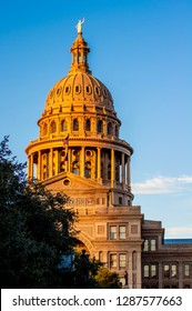 Golden hour sunlight reflects off of the front entrance and dome of the Texas state capital building in Austin with a clear blue sky in the background