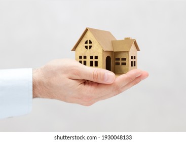 Golden House Miniature In Hand On Gray Background