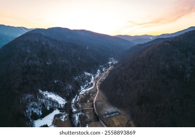 Golden hues cast across the rugged peaks of Piatra Craiului as the sun sets behind expansive mountains, revealing winding roads and serene landscapes in Brasov, Romania - Powered by Shutterstock