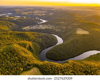 Golden hues illuminate the Vltava River as the sun sets behind rolling hills in Czechia, creating a breathtaking view of the water winding through lush forests and serene landscapes. - Powered by Shutterstock