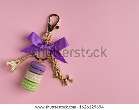 Golden key chain with golden eiffel tower, french macarons and purple bow knot. Place for text, copy space. Pink background. Gift for birthday.