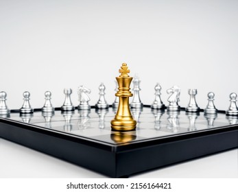 The Golden king chess piece standing on chessboard corner in front of many silver chess pieces on white background. Leadership, fighter, competition, confrontation, and business strategy concept. - Shutterstock ID 2156164421