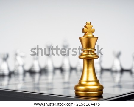 The Golden king chess piece standing on chessboard corner in front of many silver chess pieces on white background. Leadership, fighter, competition, confrontation, and business strategy concept.