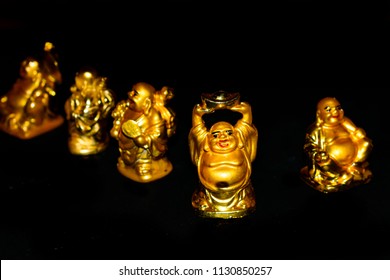 Golden Laughing Buddhas with relaxed mindset. Isolated on dark black background. Selective focus and shallow depth of field - Powered by Shutterstock