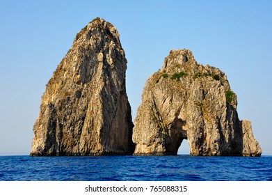 Golden light, blue sky and water frame the dramatic sea stacks of Capri, Faraglioni di Fuori (Scopolo) and Faraglioni di Mezzo (with famous archway). - Powered by Shutterstock