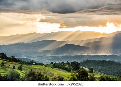 Golden light rays from raining clouds shining to the mountain with rice terrace field and hut. Sun rays over valley. Sun rays over hill. Beam of light from clouds on the mountains. Heaven in nature. 