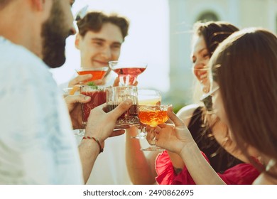 Golden light of sun enhances cheerful toast among friends, their drinks shimmering. Concept of party, Friday mood, alcohol drinks and celebration, summer holidays, relax, rest, youth. - Powered by Shutterstock