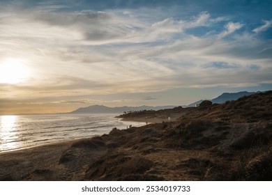 The golden light of sunset bathes the coastal dunes as distant mountains provide a stunning backdrop. The peaceful shoreline adds to the tranquil and scenic view - Powered by Shutterstock