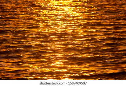 Golden Light, Sunset on water. Setting sun reflected in ripples of water. Bands of yellow and warm orange tones. Background texture.
