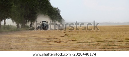 Golden linen field edge road with fast drive tractors in dust cloud on , linum harvesting in East Europe at summer day