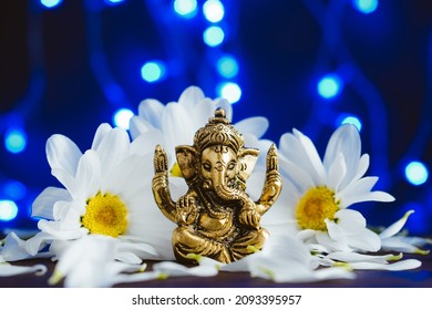 Golden lord ganesha sculpture in daisy flowers over blue illuminated background. Celebrate lord ganesha festival