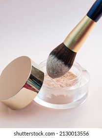 A Golden Makeup Brush Is Dipped In A Glass Jar With Powder On A Pink Background