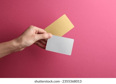 Golden and metal business cards in a female hand on a pink background