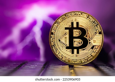 Golden metallic Bitcoin coin standing on a laptop keyboard against the background of a blurred dramatic multicolored stormy sky with lightning - Shutterstock ID 2253906903