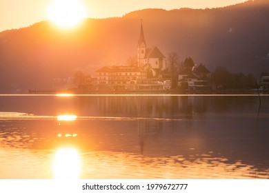 Golden morning sunrise over the pilgrim village and church of Maria Wörth on lake Wörthersee, Carinthia, Austria