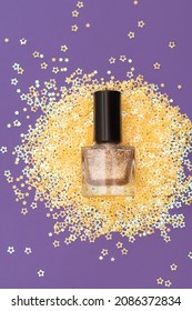 Golden nail polish bottle on purple background. Golden nail polish bottle decorated with small glitter gold stars on purple background