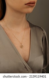 A Golden Necklace Around The Neck Of A Blonde-haired Female Model Wearing A Gray Dress.