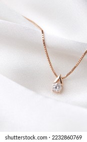Golden necklace with crystals on white silk background, rose gold, single diamond pendant. Beautiful accessories for women. Elegant jewelery gift or present for wedding or saint valentine's day.