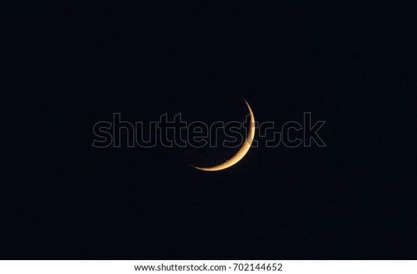 Golden\
new moon isolated on black sky, telephoto\
image.